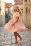 Rochie Sia roz – fetiță care se învârte pe o stradă pavată din orașul vechi